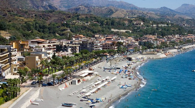 Spiaggia affollata, ombrelloni e città sullo sfondo.