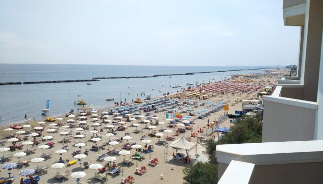 Spaggia affollata con ombrelloni bianchi e colorati.