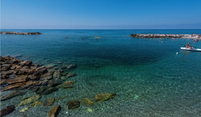 Spiaggia con mare cristallino e scogli in primo piano.
