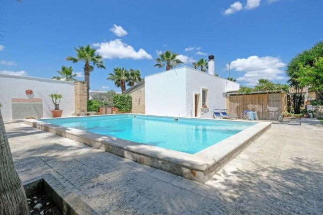 Piscina all'aperto con palme e edifici bianchi.