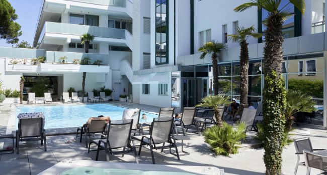 Piscina con lettini e palme accanto a un edificio.