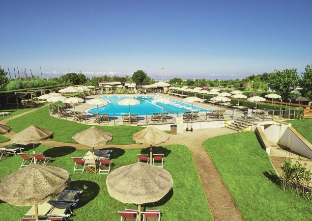 Piscina circondata da lettini e ombrelloni su un prato.