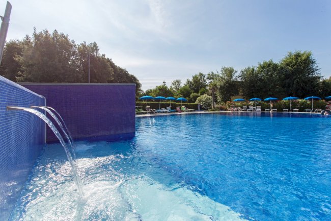 Piscina blu con fontana e ombrelloni sullo sfondo.