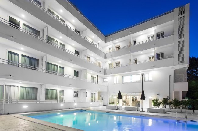 Edificio alberghiero bianco a più piani con piscina illuminata.