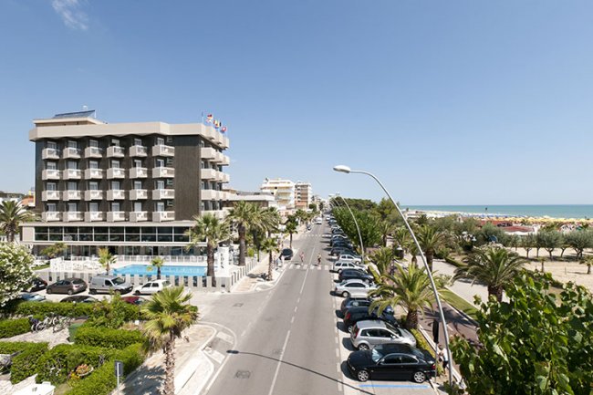 Strada con hotel, alberi e vista sul mare.