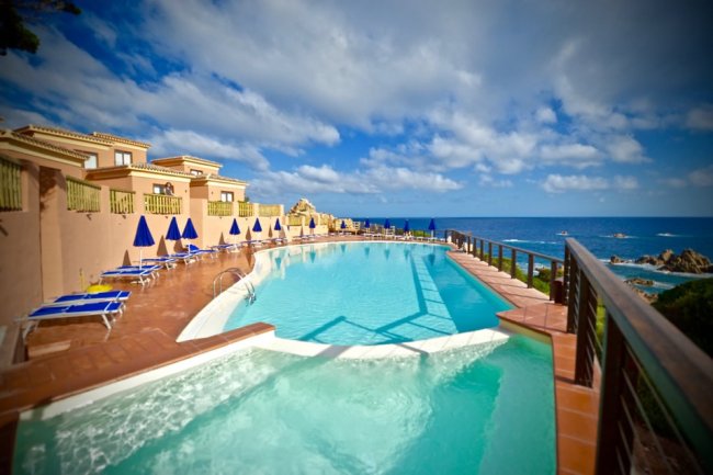 Piscina a sfioro con sedie a sdraio vista mare.