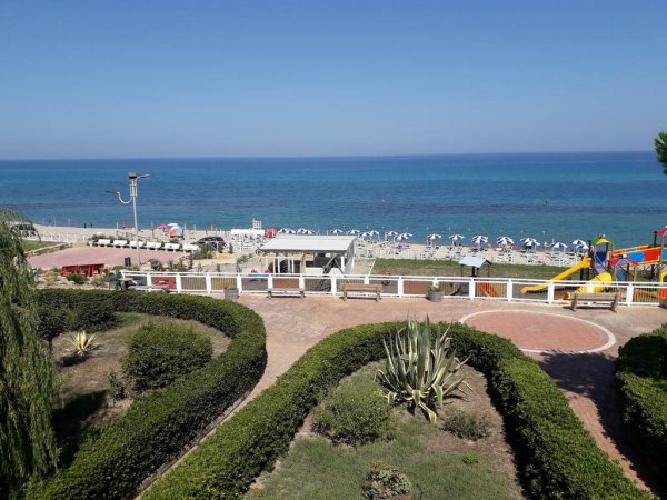 Vista sul mare con ombrelloni e giardino curato.