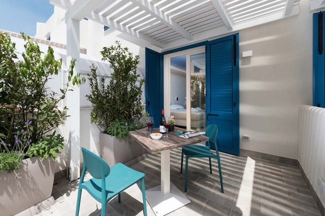 Terrazza bianca con sedie blu, tavolo e piante.