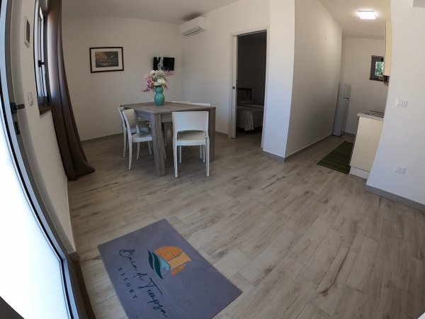 Soggiorno con tavolo, quattro sedie e pavimento in legno chiaro.