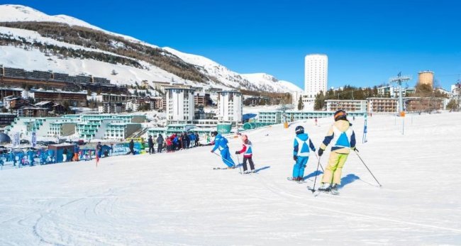 Sciatori su una pista con edifici sullo sfondo.
