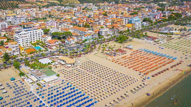 Spiaggia affollata con file di ombrelloni colorati.