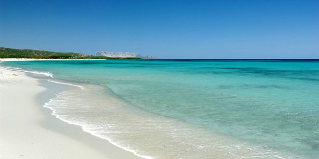 Spiaggia sabbiosa con mare cristallino e cielo blu.