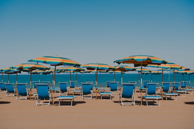Spiaggia sabbiosa con sdraio blu e ombrelloni a righe colorate.