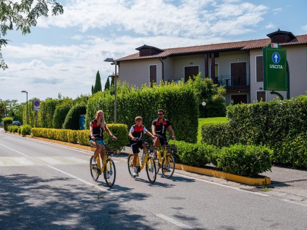 Tre persone in bicicletta su una strada davanti a edifici verdi.