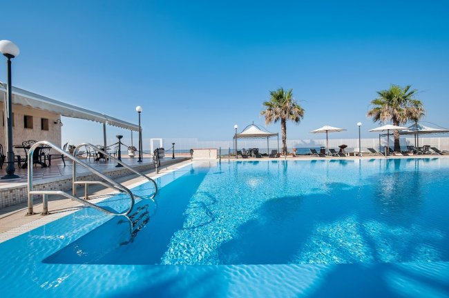 Piscina all'aperto con vista sul mare, palme e sedie a sdraio.