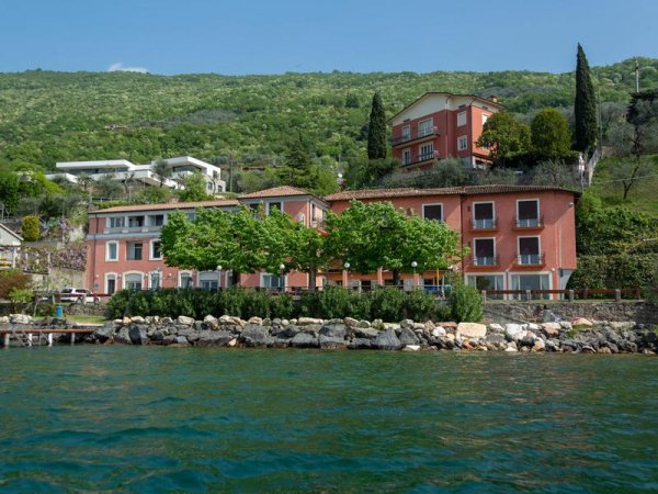 Edificio rosa fronte lago con colline verdi.