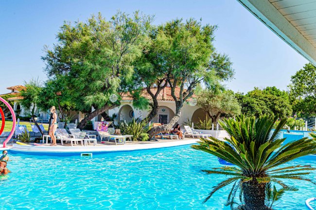 Piscina con lettini e alberi verdi.