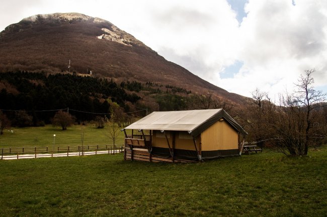 Tenda in campo verde con montagna sullo sfondo.