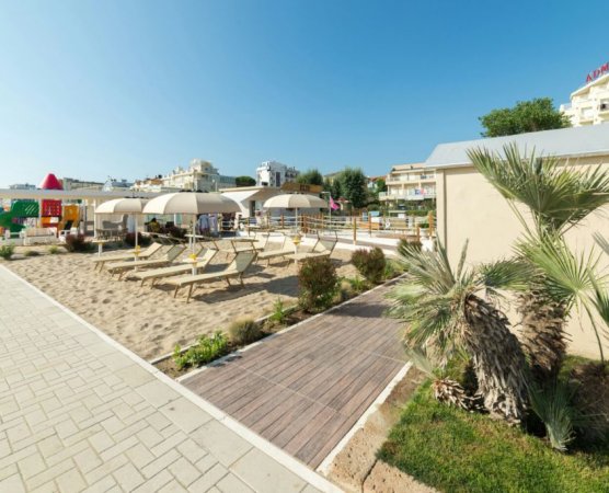 Lettini e ombrelloni su sabbia vicino a passerella di legno.