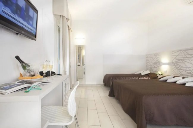 Camera d'hotel con due letti matrimoniali, TV a muro, scrivania.