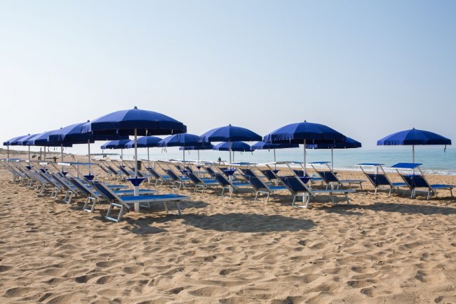 Spiaggia con sdraio e ombrelloni blu.