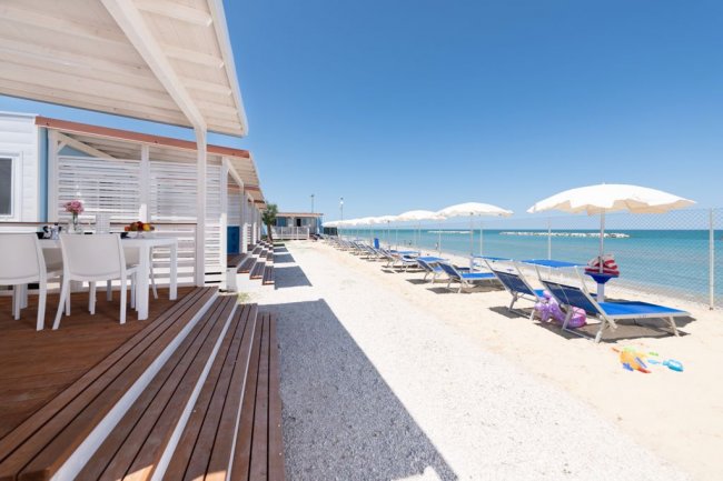 Spiaggia con sedie a sdraio e ombrelloni, accanto a una terrazza in legno.