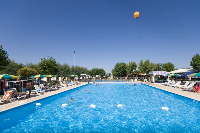 Una grande piscina all'aperto con lettini e ombrelloni colorati.