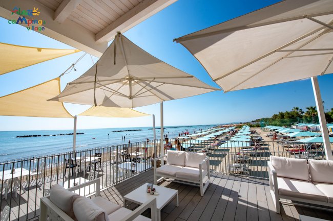 Terrazza sul mare con ombrelloni, sedie e vista su spiaggia attrezzata.