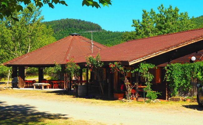 Edificio rustico con veranda, tavoli e viste su colline.