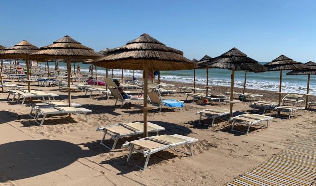 Lettini e ombrelloni vuoti su una spiaggia sabbiosa con onde in lontananza.