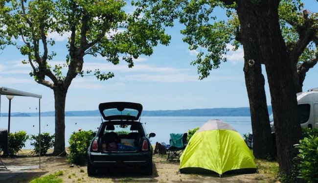 Auto e tenda vicino al lago con alberi.