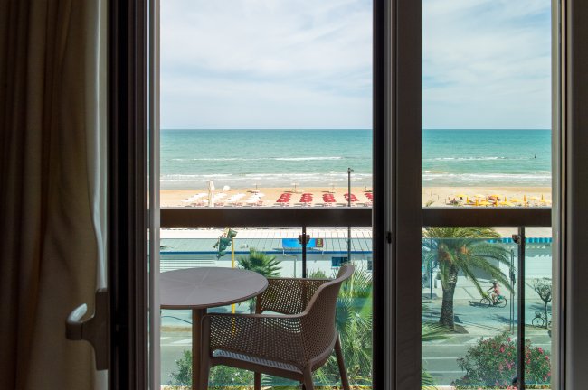 Vista sul mare dalla finestra con tavolino e sedia sul balcone.
