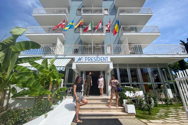 Facciata di un hotel con persone davanti e bandiere sul balcone.