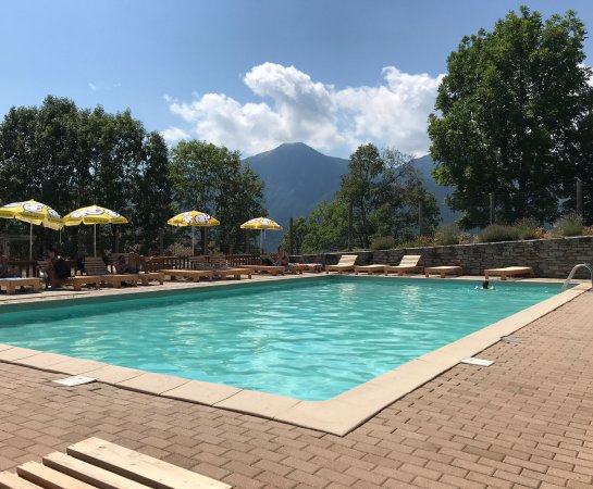 Piscina esterna con ombrelloni gialli e montagne sullo sfondo.
