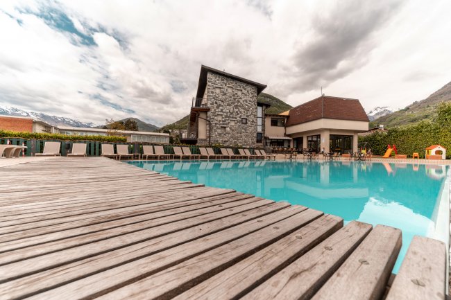 Piscina con bordo in legno e edificio in pietra sullo sfondo.