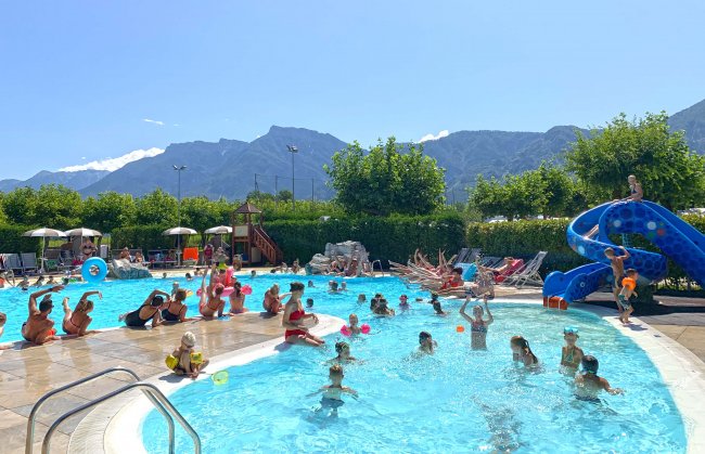 Piscina affollata di persone, montagne sullo sfondo.