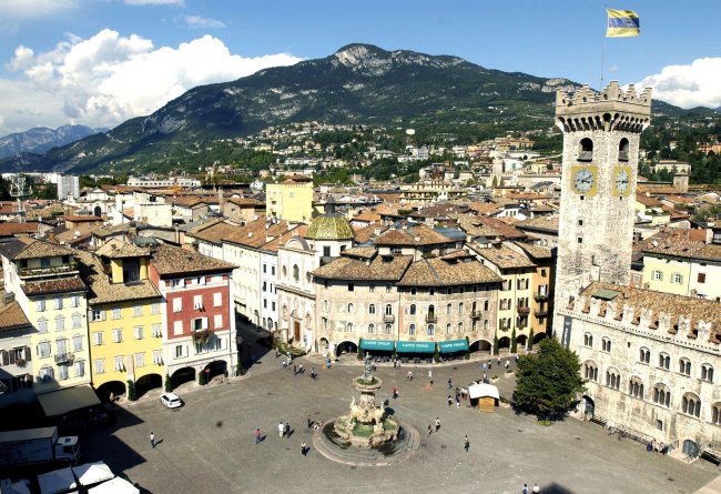Piazza con fontana e torre, circondata da edifici storici.