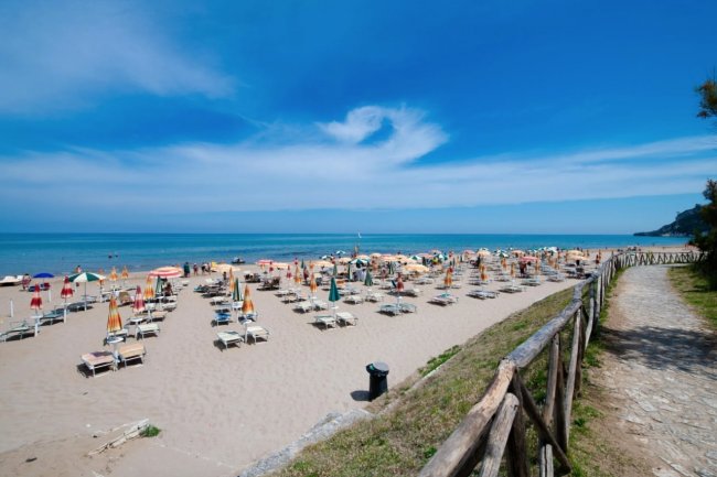 Spiaggia sabbiosa con lettini e ombrelloni colorati.