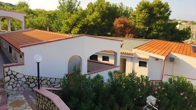 Edifici bianchi con tetti arancioni circondati da vegetazione.