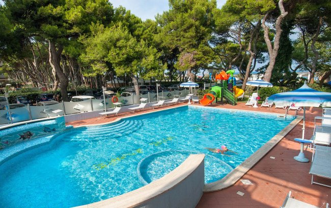 Piscina all'aperto circondata da lettini e alberi.