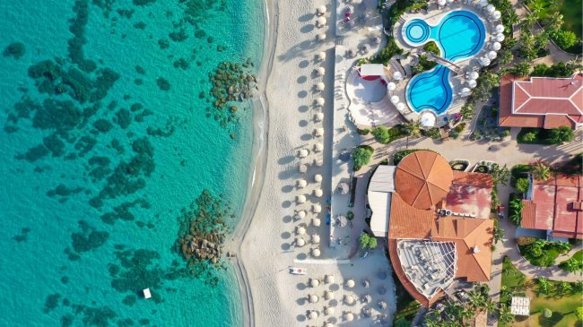 Spiaggia con mare turchese e piscina vista dall'alto.
