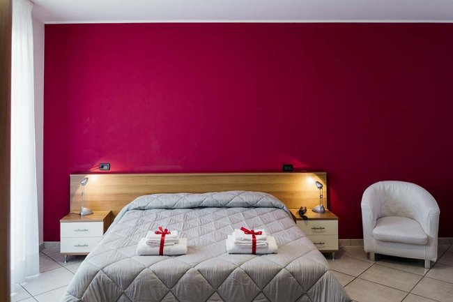 Camera da letto con parete rossa e letto matrimoniale.