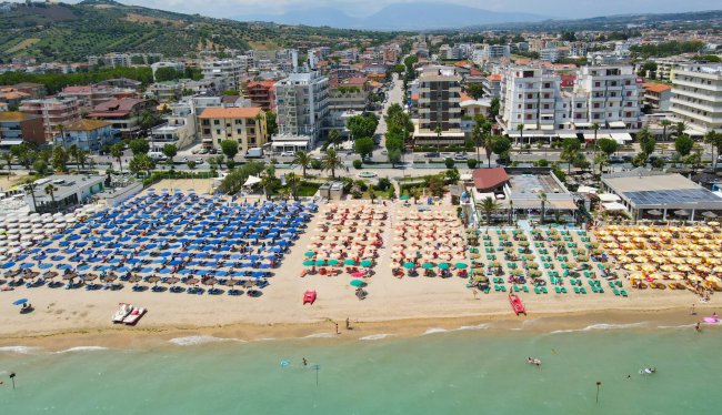 Spiaggia con ombrelloni colorati e città sullo sfondo.