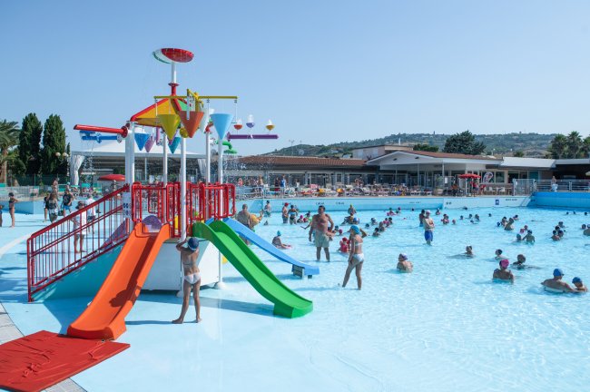 Piscina affollata con scivoli colorati e aree giochi.