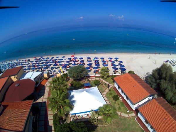 Vista dall'alto di una spiaggia con ombrelloni e mare calmo.