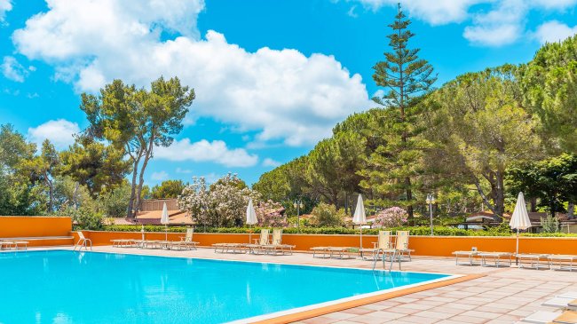 Piscina all'aperto con lettini e ombrelloni, alberi sullo sfondo.