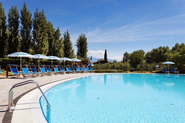 Piscina all'aperto con lettini e ombrelloni, cielo sereno.