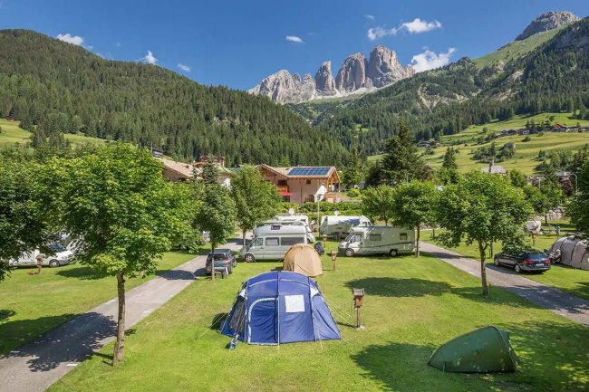 Camping con roulotte e tende, montagna sullo sfondo.