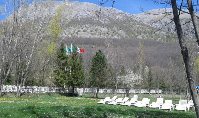 Prato con sedie a sdraio e bandiere, montagne sullo sfondo.