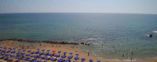 Spiaggia con ombrelloni blu e persone in acqua.